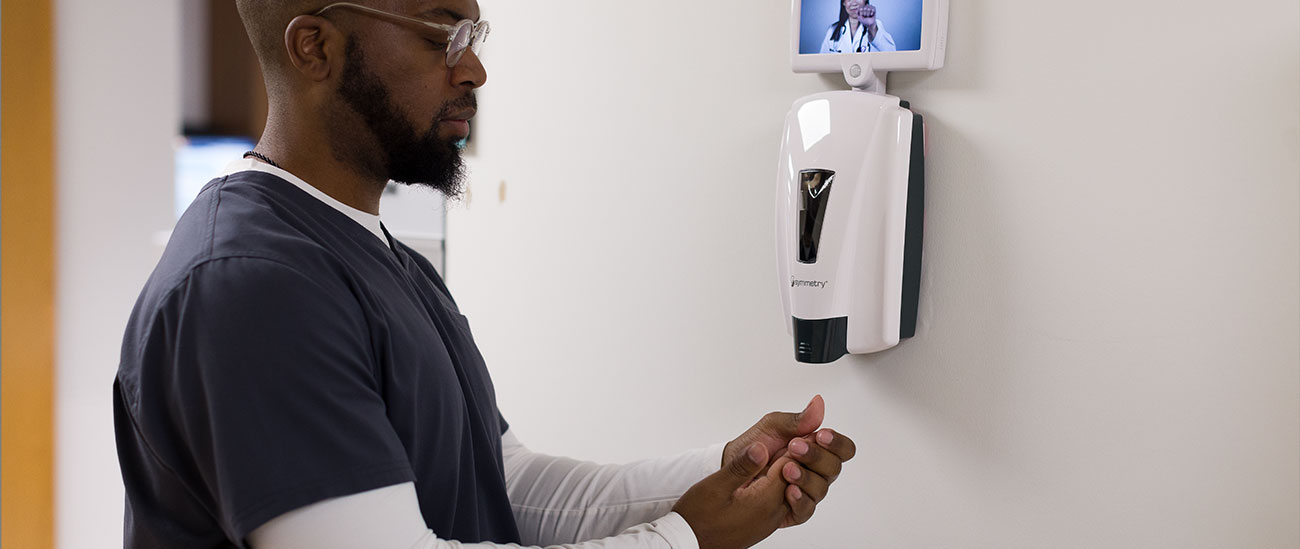 Man dressed in scrubs using an Altra dispenser on the wall